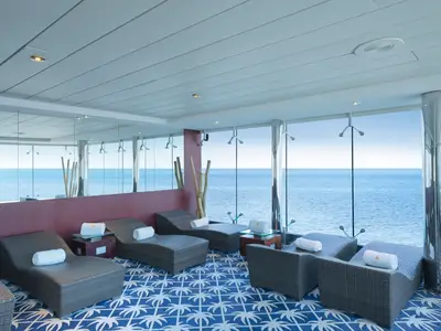 Entspannungsraum im MSC Aurea Spa an Bord der MSC Lirica. Mehrere Rattan-Liegen auf blau-weißem Teppich. Große Fenster bieten einen weiten Blick auf das offene blaue Meer.