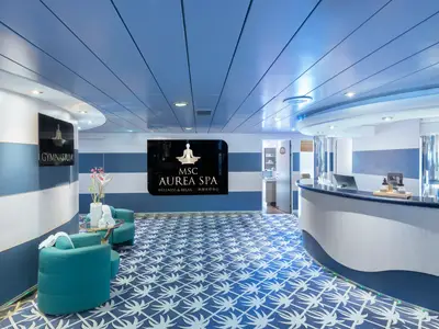 Der hellblaue und weiße Empfangsbereich des MSC AUREA SPA an Bord der MSC Lirica. Links sind bequeme Sessel, rechts ein Empfangstresen mit Produkten. Die Wände zeigen Streifen, der Boden ein Palmenmuster.