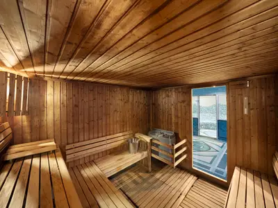 Helle Holzsauna an Bord der MSC Lirica mit Bänken, Saunaofen und Eimer. Eine offene Tür gewährt Blick auf einen blau gefliesten Wellnessbereich.