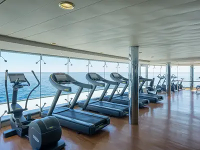 Ein heller Fitnessbereich an Bord der MSC Lirica mit einer Reihe von Laufbändern und Ellipsentrainern. Große Fensterfront bietet einen weiten Blick auf das offene Meer.