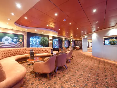 Die einladende L'Olimpiade Sporting Bar an Bord der MSC Magnifica, ausgestattet mit plueschigen roten Sofas, Sesseln, goldenen Tischen und einem Kunstwerk mit Fussbaellen.