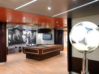 Billiardraum an Bord der MSC Magnifica mit Holzboden und oranger Decke. Eine Schwarz-Weiß-Fototapete zeigt Billardspieler. Eine beleuchtete Fußball-Stehlampe steht rechts im Bild.