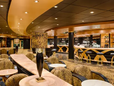 Elegante Tiger Bar an Bord der MSC Magnifica. Möbel und Dekoration im Tigermuster, eine lange goldene Bartheke mit Hockern und Spirituosenregalen sind der Blickfang.