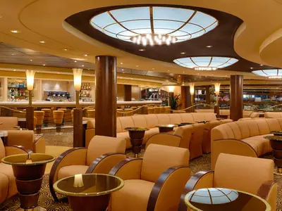 Die stilvolle Topazio Bar an Bord der MSC Magnifica mit langer Theke, Barhockern, bequemen orangefarbenen Sofas und Sesseln sowie warmem Licht.