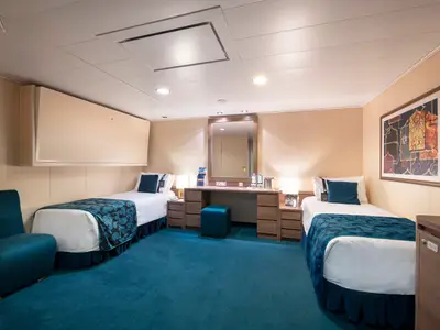 Ansicht einer modernen barrierefreien Innenkabine an Bord der MSC Magnifica. Zu sehen sind zwei Einzelbetten, ein Schminktisch mit Spiegel und ein hochgeklapptes Klappbett an der Wand. Der Raum ist in Beige- und Türkistönen gehalten.