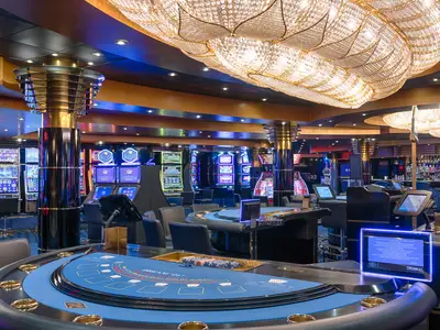 Blick in das luxuriöse Atlantic City Casino an Bord der MSC Magnifica, beleuchtet von farbigen Lichtern der Spielautomaten und glänzenden Kronleuchtern über mehreren Spieltischen.