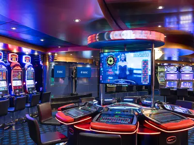 Ein lebhaft beleuchtetes Atlantic City Casino an Bord der MSC Magnifica mit zahlreichen leuchtenden Spielautomaten und modernen elektronischen Roulettetischen. Große Bildschirme zeigen Spielstände und Live-Dealer.