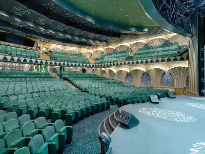 Ein großer Theatersaal, das Royal Theatre, an Bord der MSC Magnifica. Reihen grüner Samtsessel blicken auf die beleuchtete Bühne. Elegante Wände mit Muschelmotiven und Sternenlichtern.