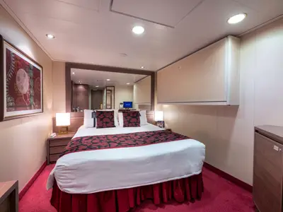 Innenkabine an Bord der MSC Magnifica. Ein Doppelbett mit roten Kissen und Überwurf steht im Zentrum. Rechts ein Fernseher auf einem Schrank, links ein großes abstraktes Kunstwerk. Die Kabine ist hell beleuchtet.