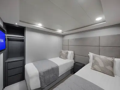 Moderne Innenkabine an Bord der MSC Magnifica. Zwei Einzelbetten, gepolstertes Kopfteil, TV und Kleiderschrank. In Grau- und Weißtönen gehalten. Ohne Personen.