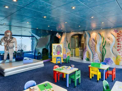 Bunter Kinderbereich an Bord der MSC Magnifica, im Unterwasser-Design mit Spieltischen und Stühlen. Eine große Glasfront bietet Meerblick.