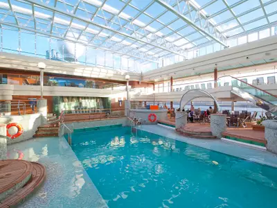 Der helle Poolbereich La Grotta Azzurra auf der MSC Magnifica mit großem Pool, Whirlpool, Liegen und Sitzbereichen unter einem weitläufigen Glasdach. Viele Personen entspannen am Pool und in den Lounges.