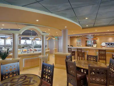 Sahara Buffet an Bord der MSC Magnifica. Elegante Tische, verzierte Stühle, Buffet mit Obst und eine Bar mit Kaffeemaschinen. Warme und einladende Atmosphäre.