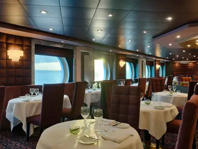 Innenansicht des eleganten Spezialitätenrestaurants Quattro Venti an Bord der MSC Magnifica mit gedeckten Tischen, bequemen Sitzen und runden Fenstern mit Blick auf das Meer.