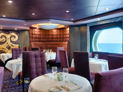 Ein stilvolles Spezialitätenrestaurant Quattro Venti an Bord der MSC Magnifica, ausgestattet mit dunkelroten Polsterbänken, lila Samtstühlen und weiss gedeckten Tischen. Grosse runde Fenster bieten einen weiten Blick auf das offene Meer.