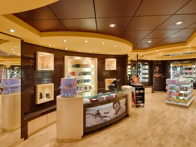 Ein eleganter Parfümerie- und Kosmetik-Shop an Bord der MSC Magnifica. Luxuriöse Markenprodukte in beleuchteten Vitrinen. Moderner Verkaufstresen. Warme Farben, ohne Personen.