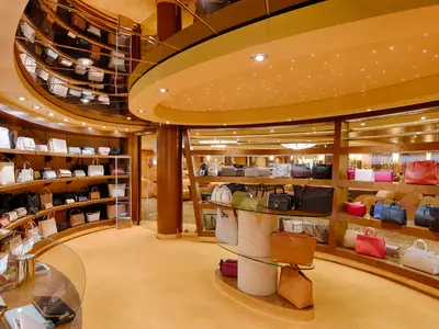 Eine Innenansicht des eleganten Accessoires-Shops an Bord der MSC Magnifica, der eine Vielzahl von Handtaschen auf geschwungenen Holzregalen und Glasvitrinen präsentiert. Das warme Licht akzentuiert die luxuriöse Atmosphäre.