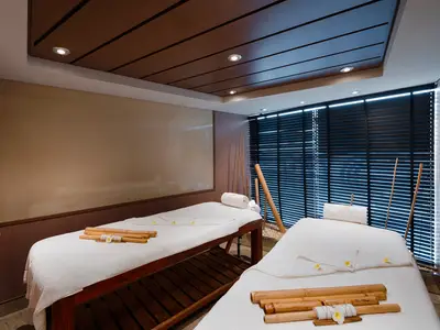Zwei weiß bezogene Massageliegen stehen in einem eleganten Spa-Raum an Bord der MSC Magnifica. Bambusstangen, Bademantel und eine dunkle Jalousie sind sichtbar.