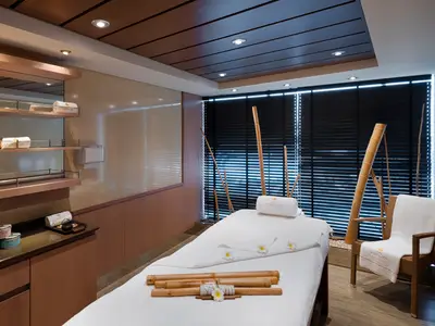 Ein ruhiger Behandlungsraum im MSC Aurea Spa der MSC Magnifica mit Massageliege, Bambusdekoration, Regalen und Pflegeprodukten.