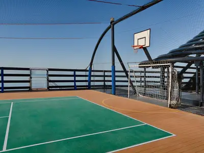 Sportplatz an Deck der MSC Magnifica unter blauem Himmel. Mit grünem Feld, Basketballkorb und Fußballtor, umgeben von Netzen.