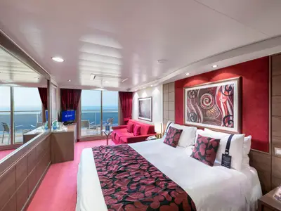 Geräumige Balkonkabine an Bord der MSC Magnifica mit einem großen Doppelbett, einem roten Sofa und einem Balkon mit Blick auf das offene Meer bei Tageslicht.