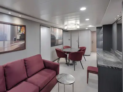 Blick in den eleganten Wohnbereich einer Suite an Bord der MSC Magnifica. Ein weinrotes Sofa, ein Esstisch mit vier Stühlen und ein Sideboard mit Spiegel prägen den Raum.