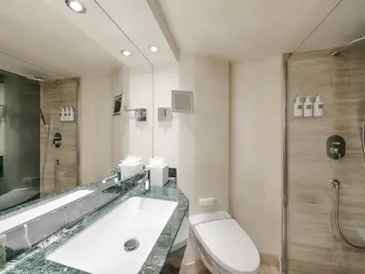 Modernes Bad in einer MSC Yacht Club Deluxe Suite an Bord der MSC Magnifica. Heller Raum mit Waschtisch, Spiegel, Toilette und Duschkabine mit Regendusche.