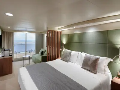 Eine geräumige Balkonsuite an Bord der MSC Magnifica mit großem Doppelbett, grünem Sofa, Kaffeemaschine und Meerblick vom Balkon.