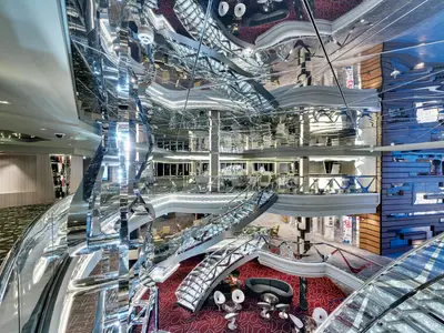 Ein imposanter Blick in das moderne Infinity Atrium der MSC Meraviglia. Glänzende Treppen verbinden mehrere Ebenen mit stilvollen Lounge-Bereichen. Der Raum ist von reflektierenden Oberflächen und indirekter Beleuchtung geprägt.