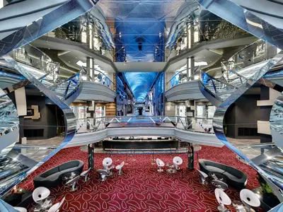 Blick ins mehrstöckige, futuristische Infinity Atrium der MSC Meraviglia mit glitzernden Treppen, Geschäften und Lounge-Bereich auf rotem Teppich.