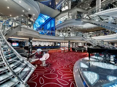 Das luxuriöse Infinity Atrium der MSC Meraviglia mit glitzernder Swarovski-Kristall-Wendeltreppe, Rezeption, Lounges und einem Flügel auf rotem Teppichboden.