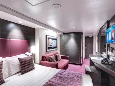 Moderne Premium-Balkonkabine an Bord der MSC Meraviglia mit Doppelbett, Sofa, Schreibtisch und TV. Dunkles Holz und violetter Teppich.