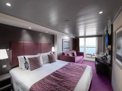 Eine moderne Balkonkabine an Bord der MSC Meraviglia mit einem Doppelbett, lila Akzenten, einem Sofa und einem Balkon mit Blick auf das Meer.