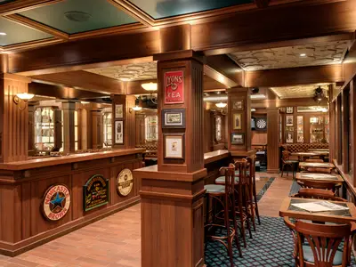 Das Brass Anchor Pub der MSC Meraviglia: Holztäfelung, Bar, Tische, Stühle und Vintage-Dekoration schaffen eine gemütliche Atmosphäre. Ein Dartboard ist sichtbar.