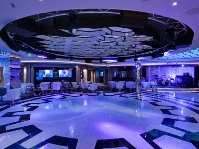 Innenansicht der Meraviglia Bar & Lounge an Bord der MSC Meraviglia mit großer Tanzfläche, Bühne mit Schlagzeug und schicken Sitzbereichen, beleuchtet in Lila und Blau.