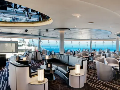 Sky Lounge an Bord der MSC Meraviglia. Raum mit Sesseln und Sofas in Grau. Große Fenster mit Meerblick. Beleuchtung und Deckenarchitektur prägen das Ambiente.