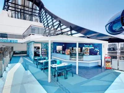 Die Polar Bar an Bord der MSC Meraviglia ist in hellen Blau- und Weisstönen gestaltet und verfügt über eine Bar und Tische. Im Hintergrund ist eine Wasserrutsche und die Skyline sichtbar. Der Stil erinnert an Eisberge.