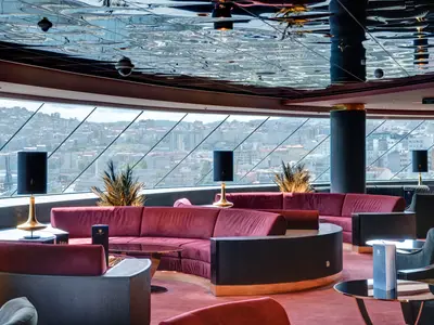 Luxuriöse Top Sail Lounge an Bord der MSC Meraviglia. Rote Samtsofas, Tische und Lampen. Große Fenster mit Blick auf eine Stadt. Die Decke ist verspiegelt.