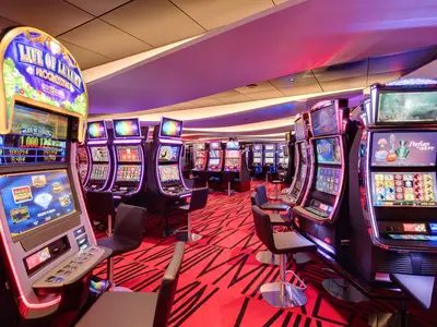 Casino Imperiale an Bord der MSC Meraviglia. Reihen von leuchtenden Spielautomaten auf rotem Teppich mit Barhockern. Moderne und lebhafte Spielatmosphäre.