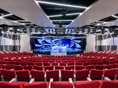 Innenansicht des modernen Broadway Theatre an Bord der MSC Meraviglia. Leere rote Sitze und eine beleuchtete Bühne mit Musikinstrumenten und einem grossen LED-Bildschirm sind zu sehen.