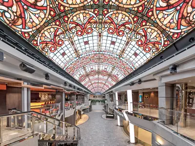 Blick in die helle 'Galleria Meraviglia' der MSC Meraviglia. Die LED-Decke simuliert ein Buntglasdach. Geschäfte und Restaurants säumen die Promenade auf mehreren Ebenen.