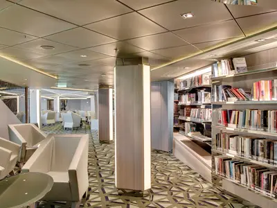 Blick in die helle und moderne Bibliothek der MSC Meraviglia, die zum Lesen und Entspannen einlädt. Zahlreiche Bücherregale mit Büchern und bequeme Sessel sind zu sehen.