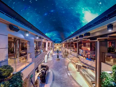 Die weitläufige Galleria Meraviglia der MSC Meraviglia bei Abendstimmung, beleuchtet von einem gewölbten LED-Himmel, der eine sternenklare Nacht simuliert. Entlang der Promenade befinden sich Geschäfte, Bars und Sitzbereiche.