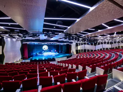 Das moderne Broadway Theatre an Bord der MSC Meraviglia. Viele rote Sitze richten sich zur hell beleuchteten Bühne. Moderne Lichtinstallationen an Decke und Wänden.