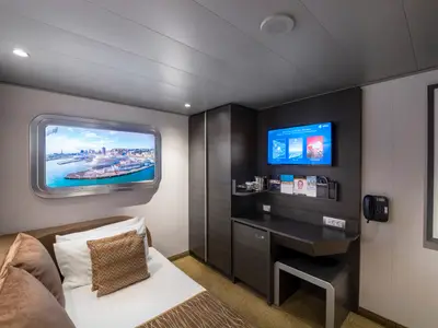 Moderne Innenkabine an Bord der MSC Meraviglia mit Sofa-Bett, virtuellem Bullauge und einem Arbeitsbereich mit TV. Einrichtung in dunklen Holztönen und neutralen Farben.