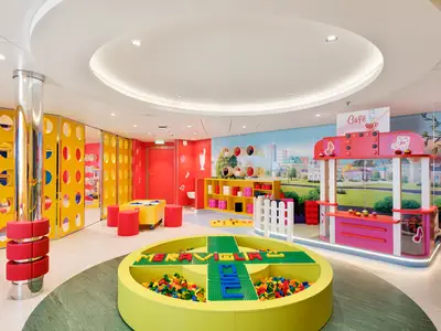 Ein farbenfroher LEGO-Kinderbereich an Bord der MSC Meraviglia mit einem großen Bausteinbecken, Spieltischen und einem Café-Stand vor einer Stadtmural.
