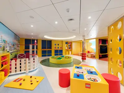 Der farbenfrohe LEGO Mini Club an Bord der MSC Meraviglia zeigt helle Räume mit diversen Spielstationen, Bausteinen und einem runden Baubereich. Bunte LEGO-Städte-Motive zieren die Wände.