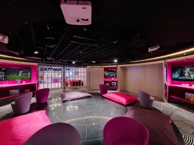 Der moderne Teen Club der MSC Meraviglia: Bildschirme zeigen Videospiele, umgeben von gemütlichen Sitzsäcken und Sesseln in leuchtendem Magenta und Lila. Eine farbenfrohe und einladende Atmosphäre.