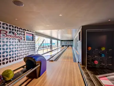 Blick auf die Bowlingbahn an Bord der MSC Meraviglia mit zwei Bahnen, Ballablage und Blick auf das Meer durch Fenster. Die Wände sind modern gestaltet.
