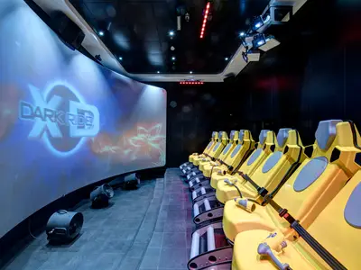 Im 4D-Kino des XD Dark Ride an Bord der MSC Meraviglia sind Reihen von gelb-grauen Bewegungssitzen vor einer großen, gekrümmten Leinwand mit der Aufschrift "XD DARK RIDE" zu sehen. Diverse Lichtinstallationen und Effektgeräte sind ebenfalls erkennbar.